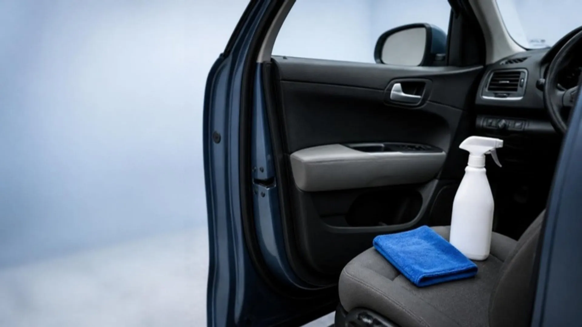 Open driver door showing a black and gray door panel, with a white spray bottle and a blue microfiber towel on the seat